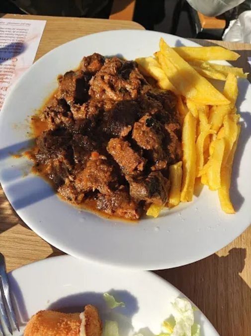 Un plato blanco cubierto con carne y papas fritas sobre una mesa.