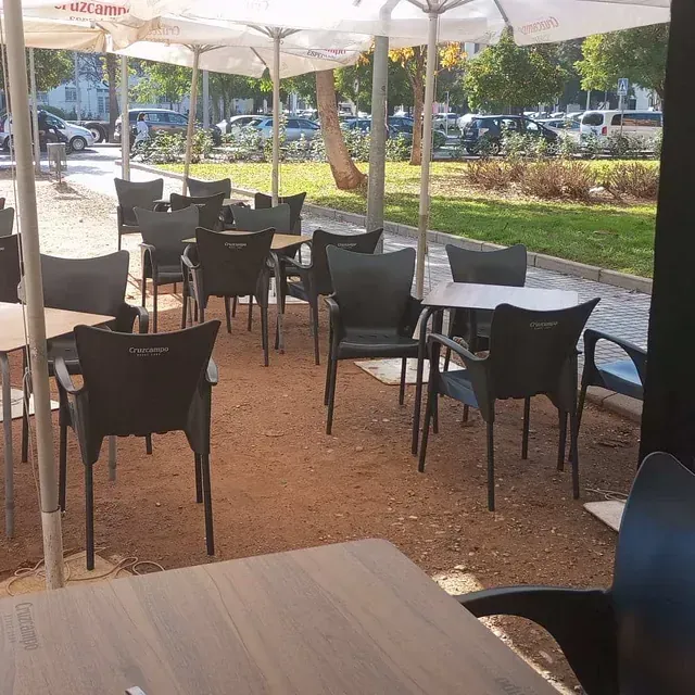 Una fila de mesas y sillas bajo sombrillas en un parque.