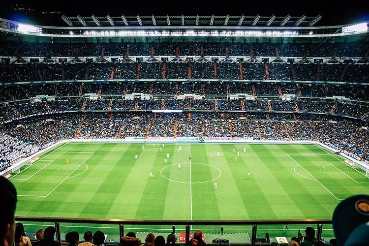 Estadio de fútbol repleto de espectadores, visto desde detrás de la portería sobre un césped de un verde brillante.