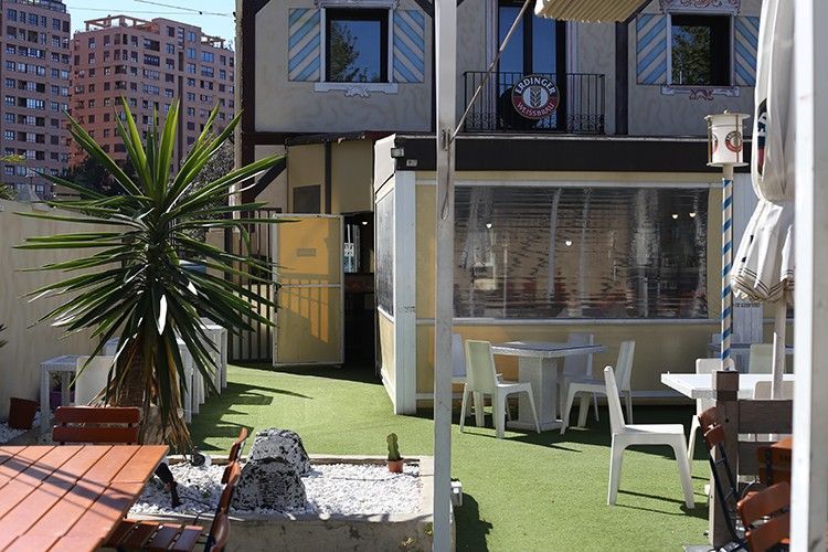 Patio trasero con sillas blancas, césped verde, plantas en macetas y la fachada de un apartamento de dos plantas.