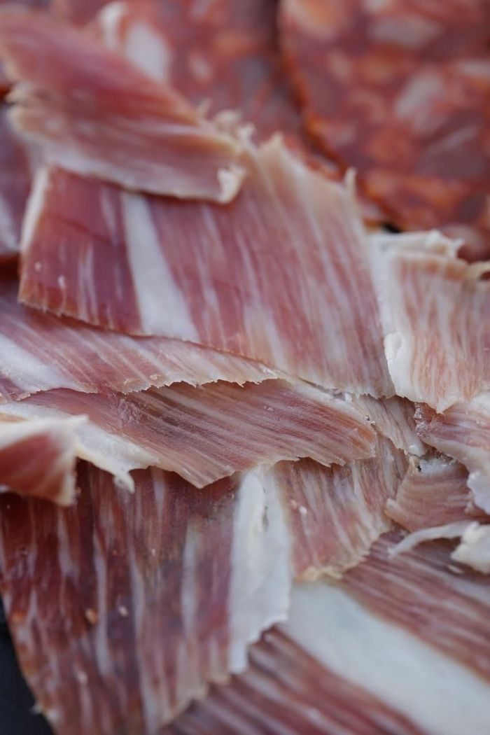 Primer plano de finas lonchas de carne curada rosada y blanca apiladas en un montón.