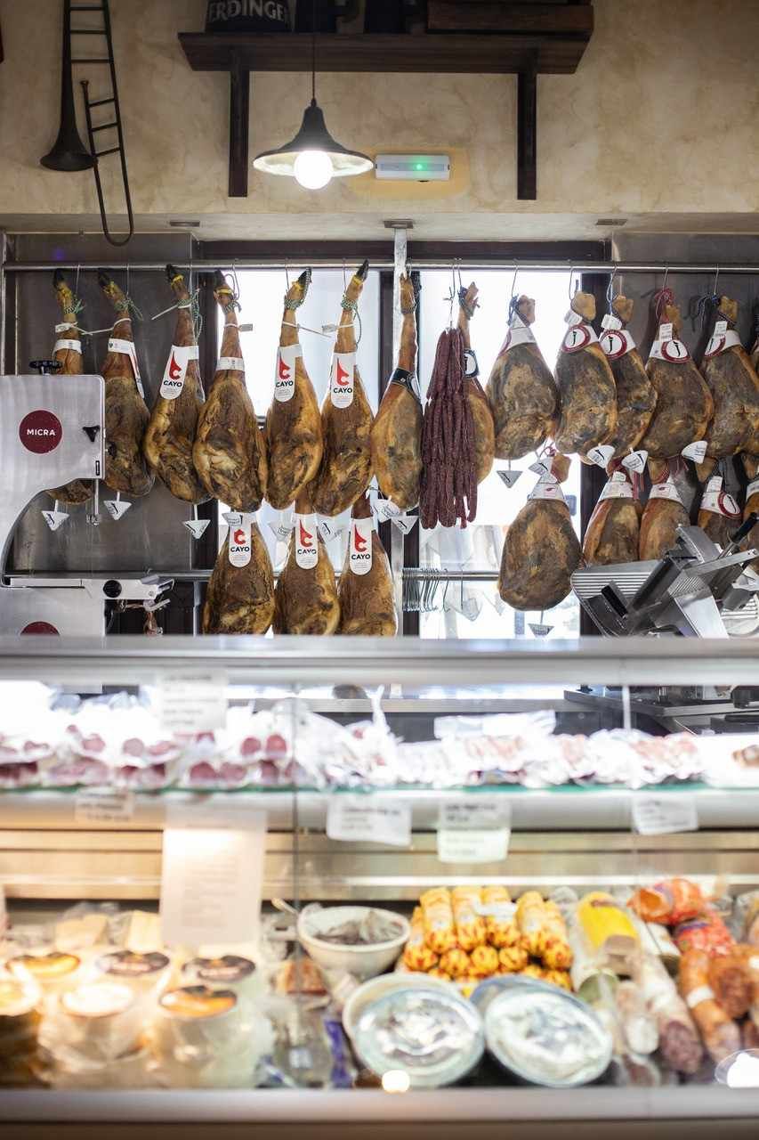En un mercado, se exhiben embutidos colgantes, charcutería, mariscos y comidas preparadas.
