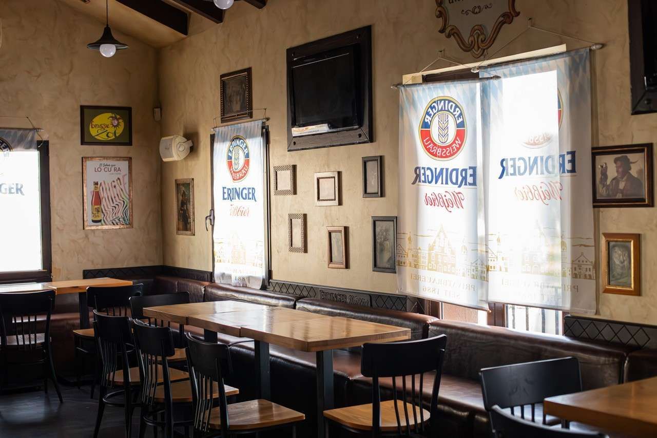 Interior vacío de un restaurante con mesas y sillas de madera, y ventanas iluminadas por el sol.