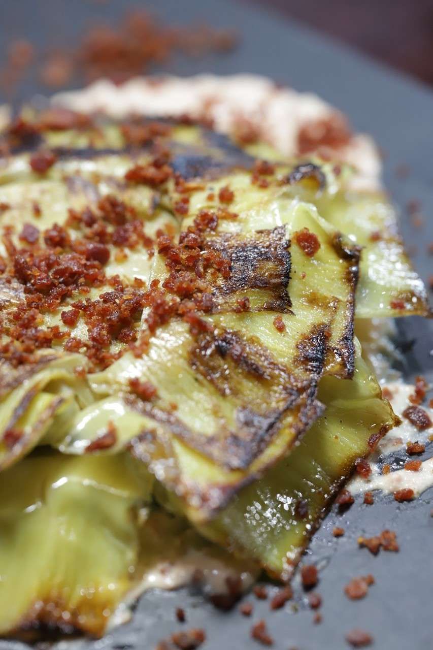 Primer plano de una comida en capas cubierta con salsa cremosa y migas crujientes en un plato.