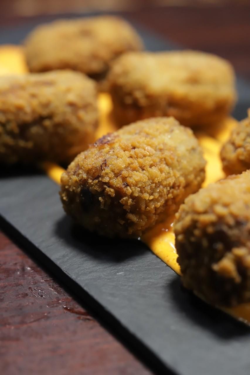 Croquetas empanizadas sobre una bandeja de pizarra negra, con una guarnición dorada debajo.