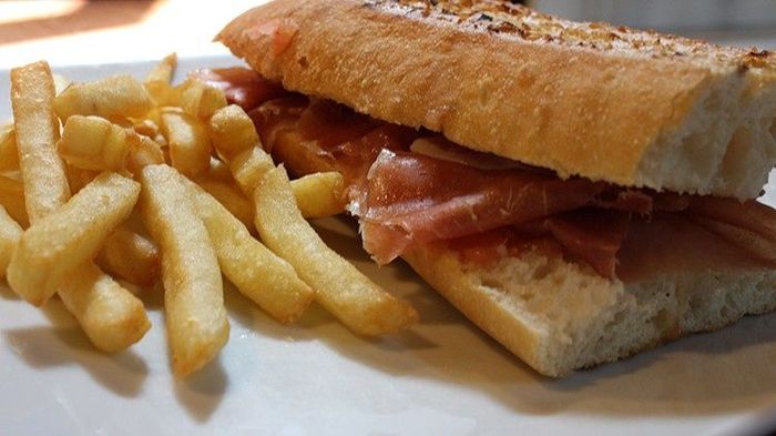 Sándwich con carne en rodajas y papas fritas en un plato blanco.