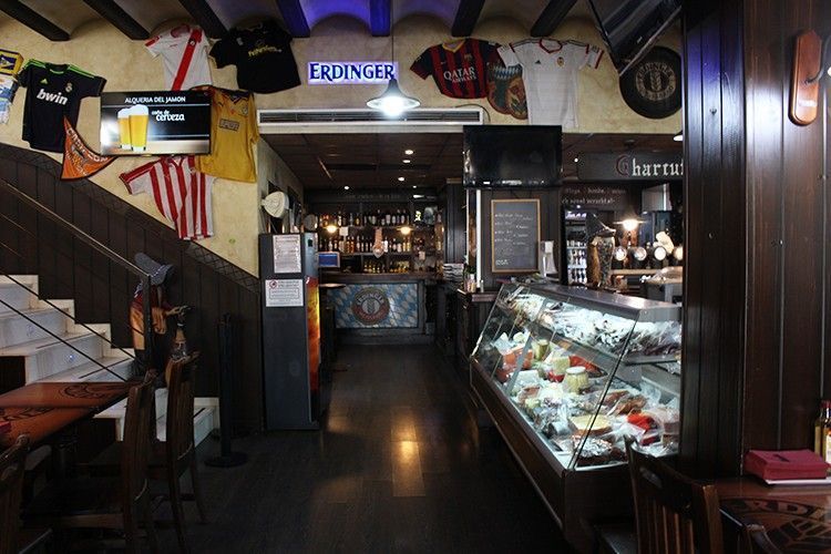 Interior de bar estrecho con luces tenues, vitrina de postres de cristal y mesas a lo largo de un pasillo oscuro.