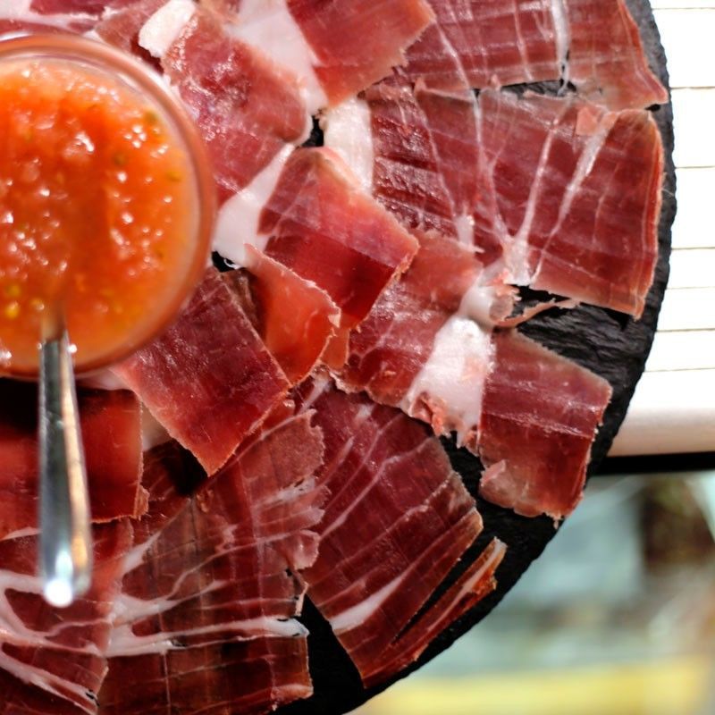 Jamón curado cortado en lonchas finas en una fuente con una cucharada de salsa rojo anaranjada.