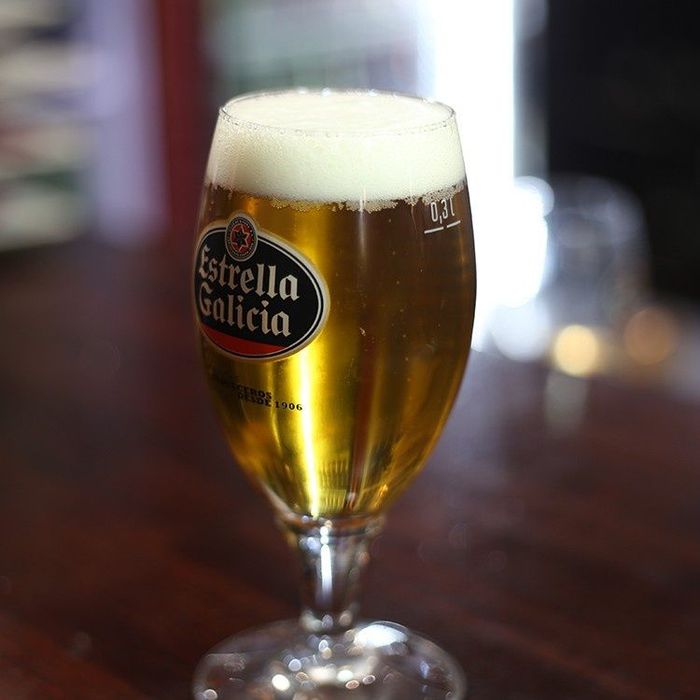 Cerveza dorada en una copa con tallo y etiqueta de Estrella Galicia en la barra.
