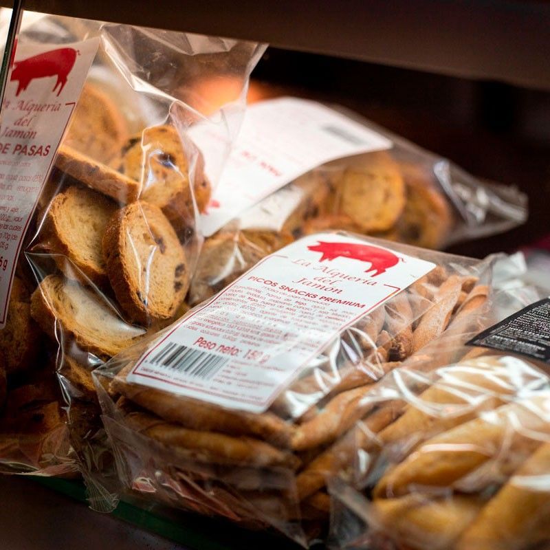 Bolsas de plástico transparente con pan de molde y pasteles, con etiquetas blancas, en un estante.