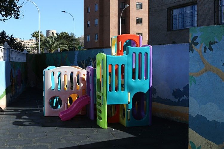 Estructura de escalada y tobogán coloridos en un área de juegos al aire libre junto a un edificio.