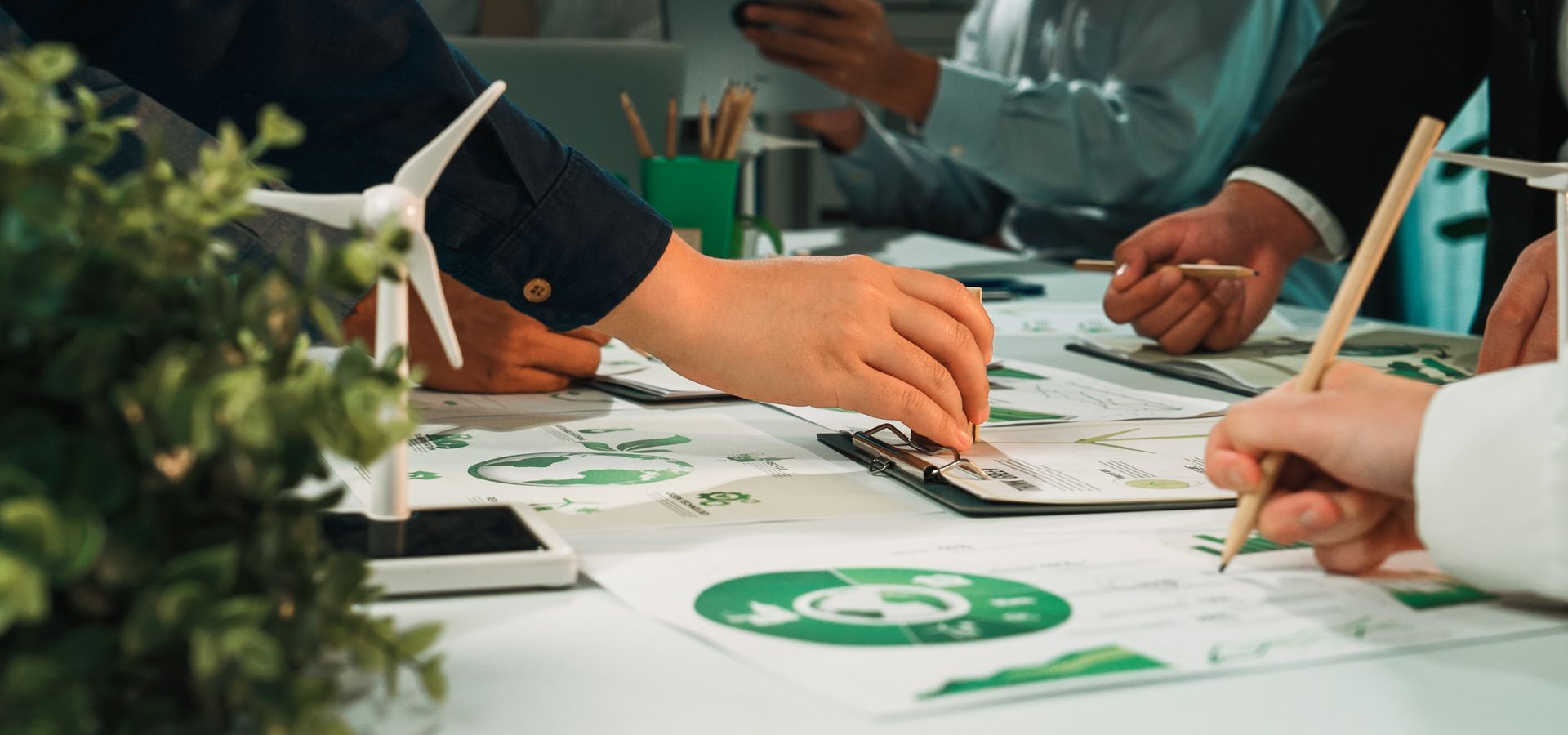 Des personnes travaillent ensemble autour d'une table avec des graphiques et une maquette d'éolienne, dans le domaine des énergies vertes.
