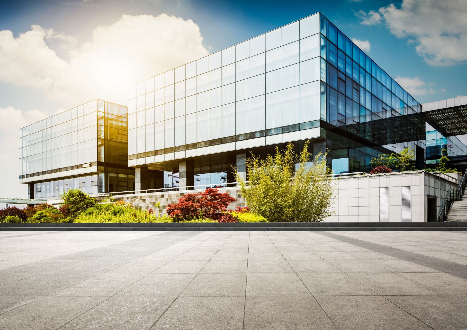 Bâtiment moderne en verre avec un ciel lumineux et un aménagement paysager en façade.