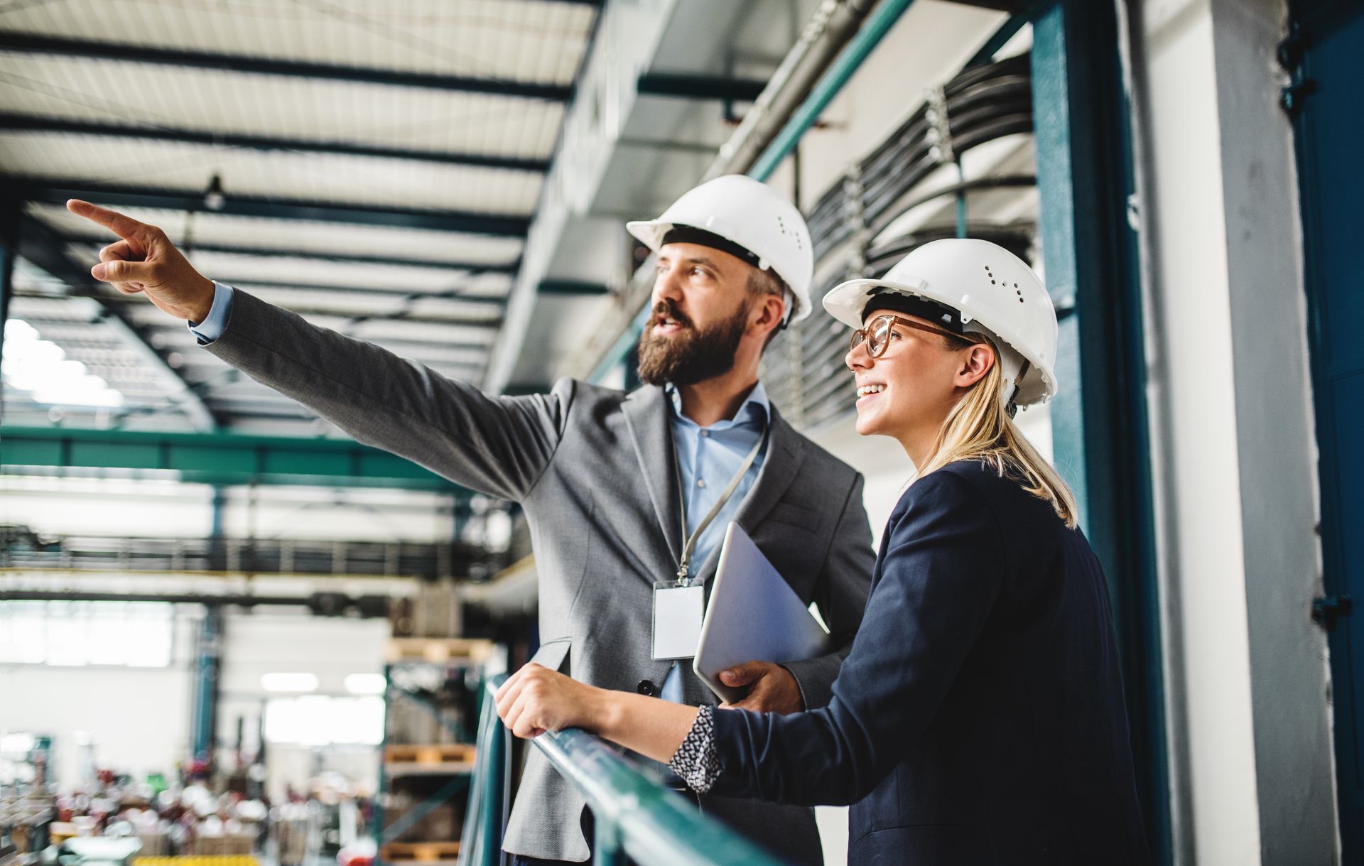 Deux personnes portant des casques de chantier dans une usine, l'une d'elles pointant du doigt, observant un équipement.