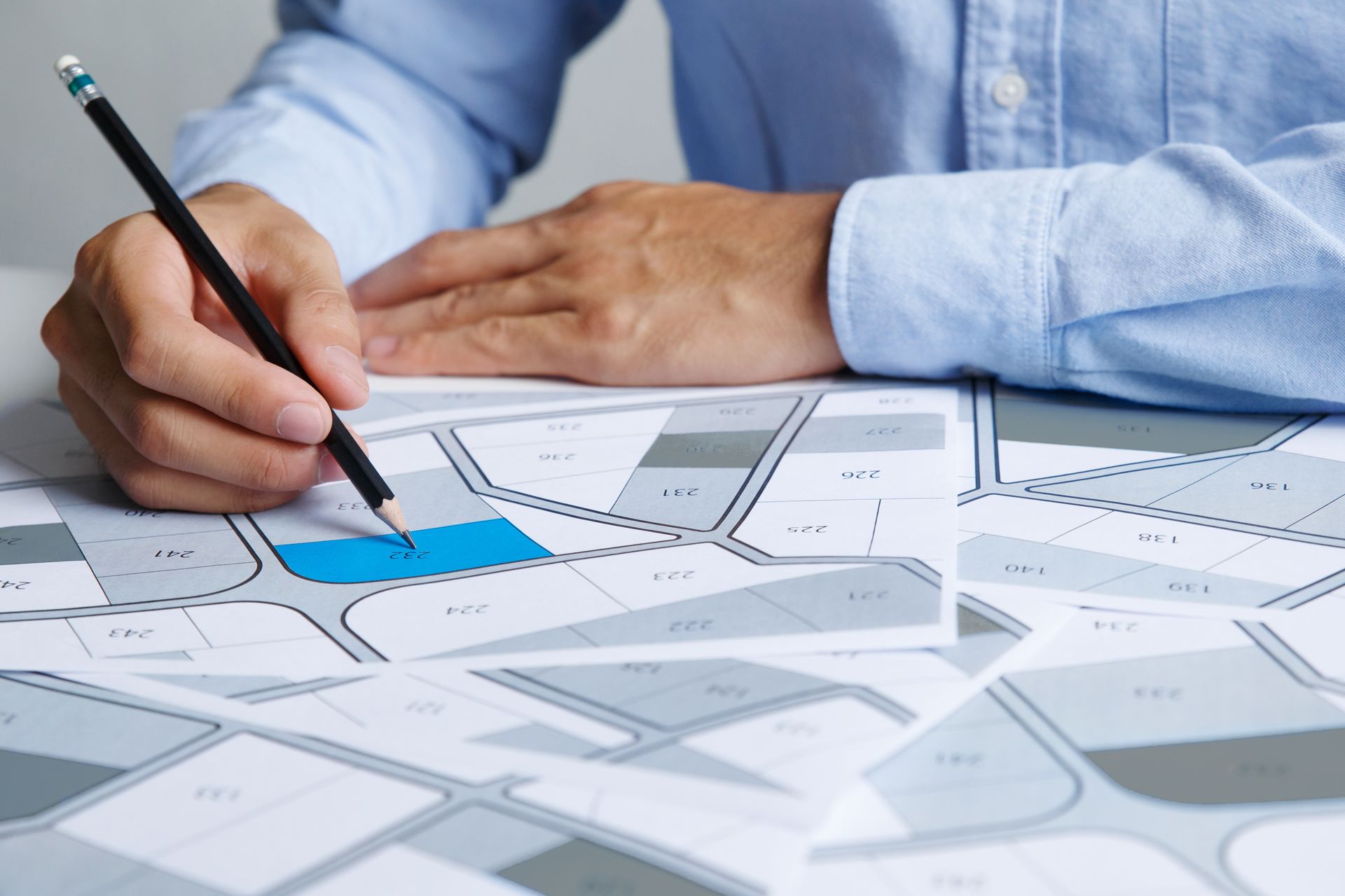 Une personne en chemise bleue dessine au crayon sur une carte, en surlignant une zone bleue.