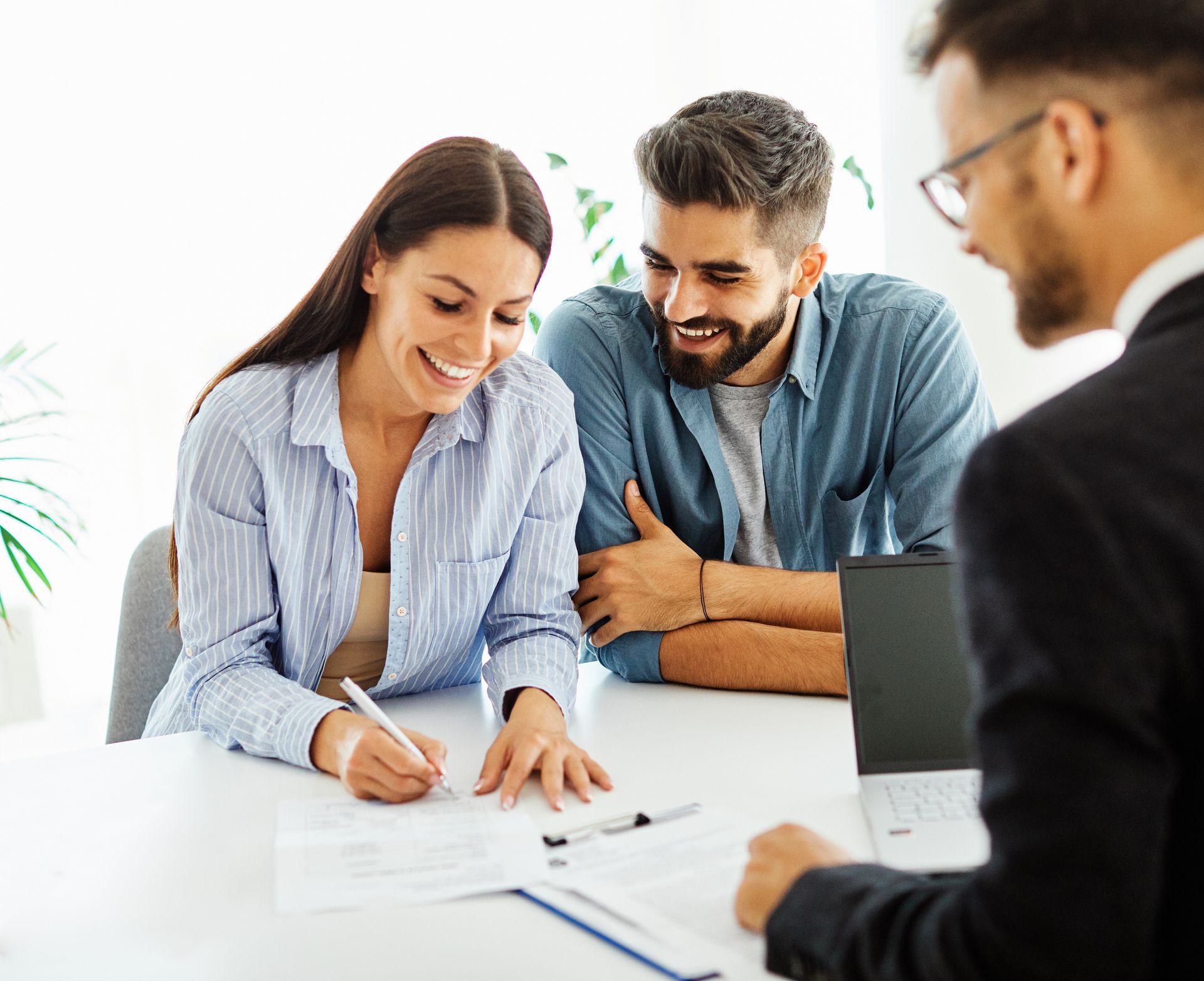 Un couple signe des documents avec un conseiller à un bureau, tout sourire.