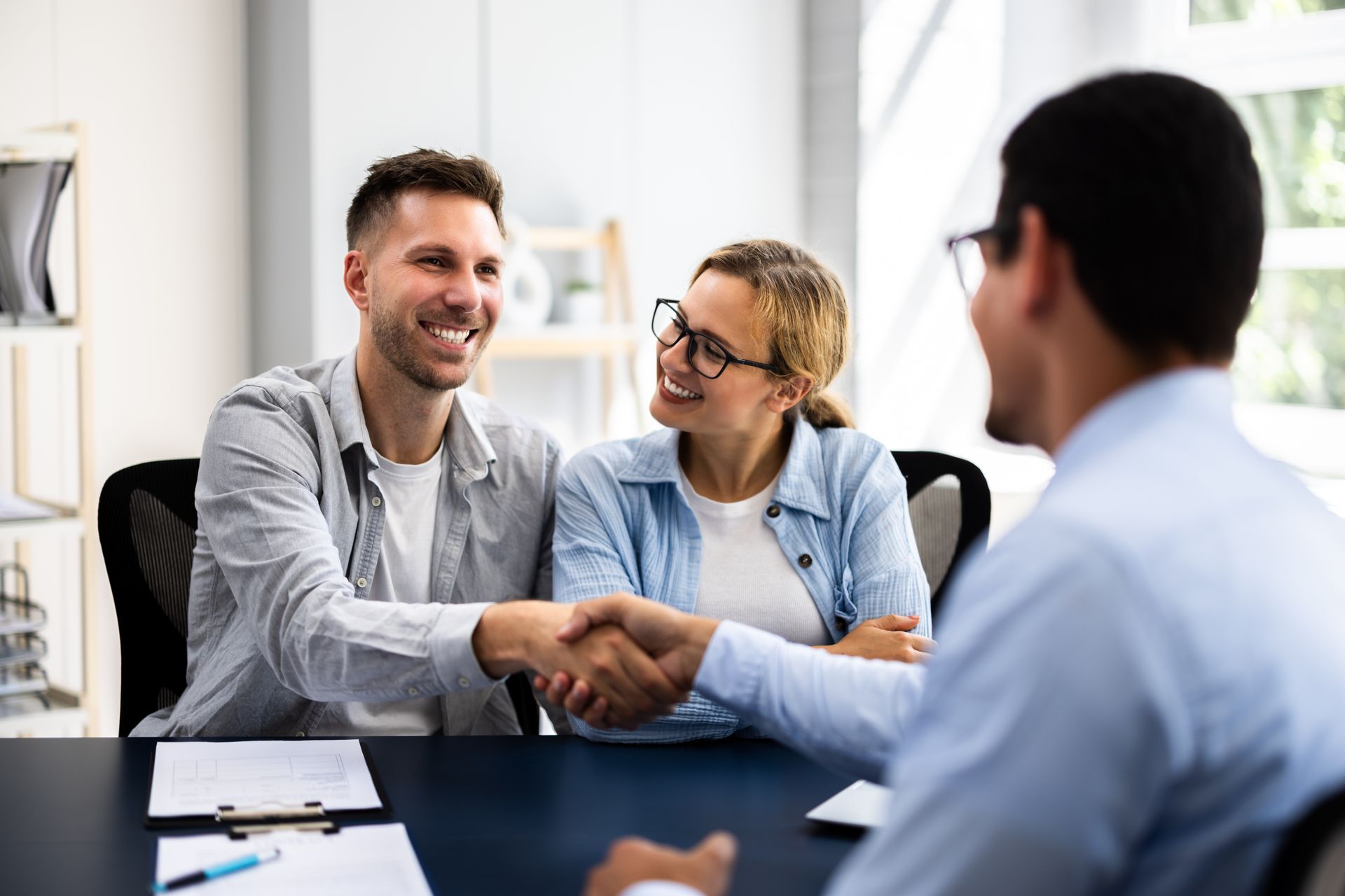 Un couple serre la main d'un homme assis à un bureau. Ils sourient tous les deux.
