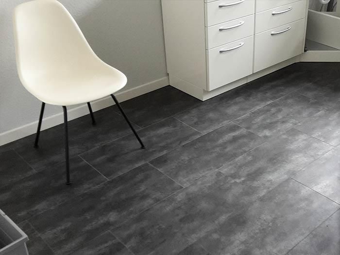 Ein weißer Stuhl steht auf einem schwarz gefliesten Boden neben einem weißen Schrank.