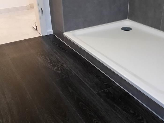 Ein Badezimmer mit schwarzem Holzboden und weißer Duschkabine.