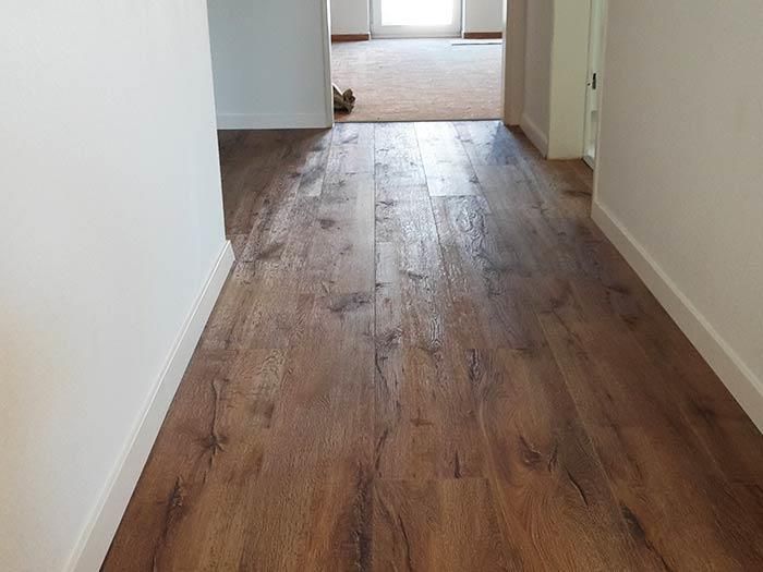 Ein Flur mit Holzboden und weißen Wänden, der zu einem Wohnzimmer führt.