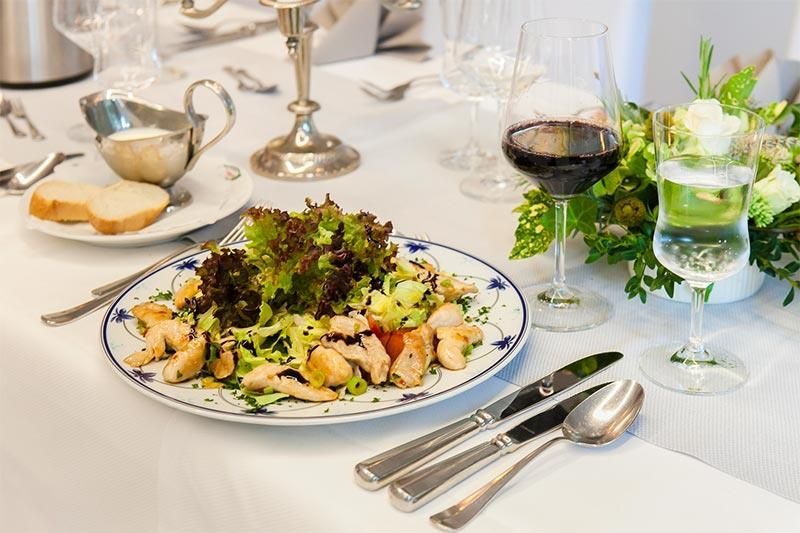 Ein Teller mit Essen steht neben einem Glas Wein auf einem Tisch.