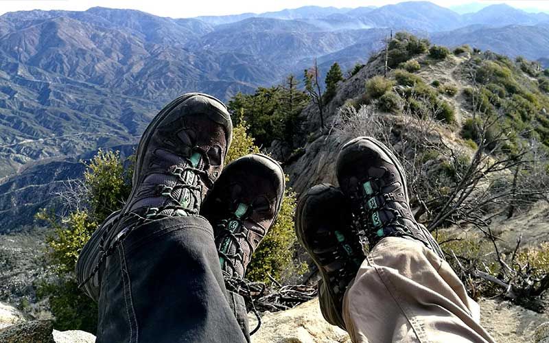 Eine Person in Wanderschuhen sitzt auf einem Berggipfel.