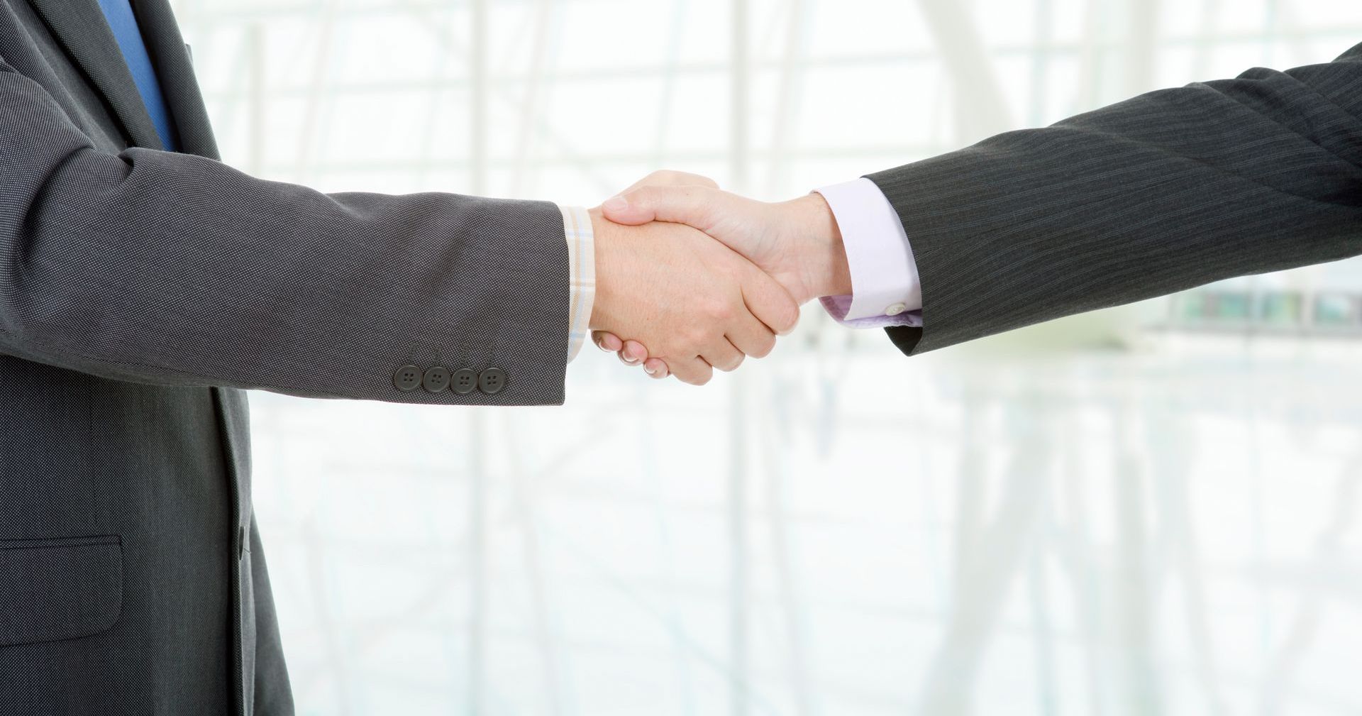 Zwei Männer in Anzügen schütteln sich die Hände in einem Bürogebäude