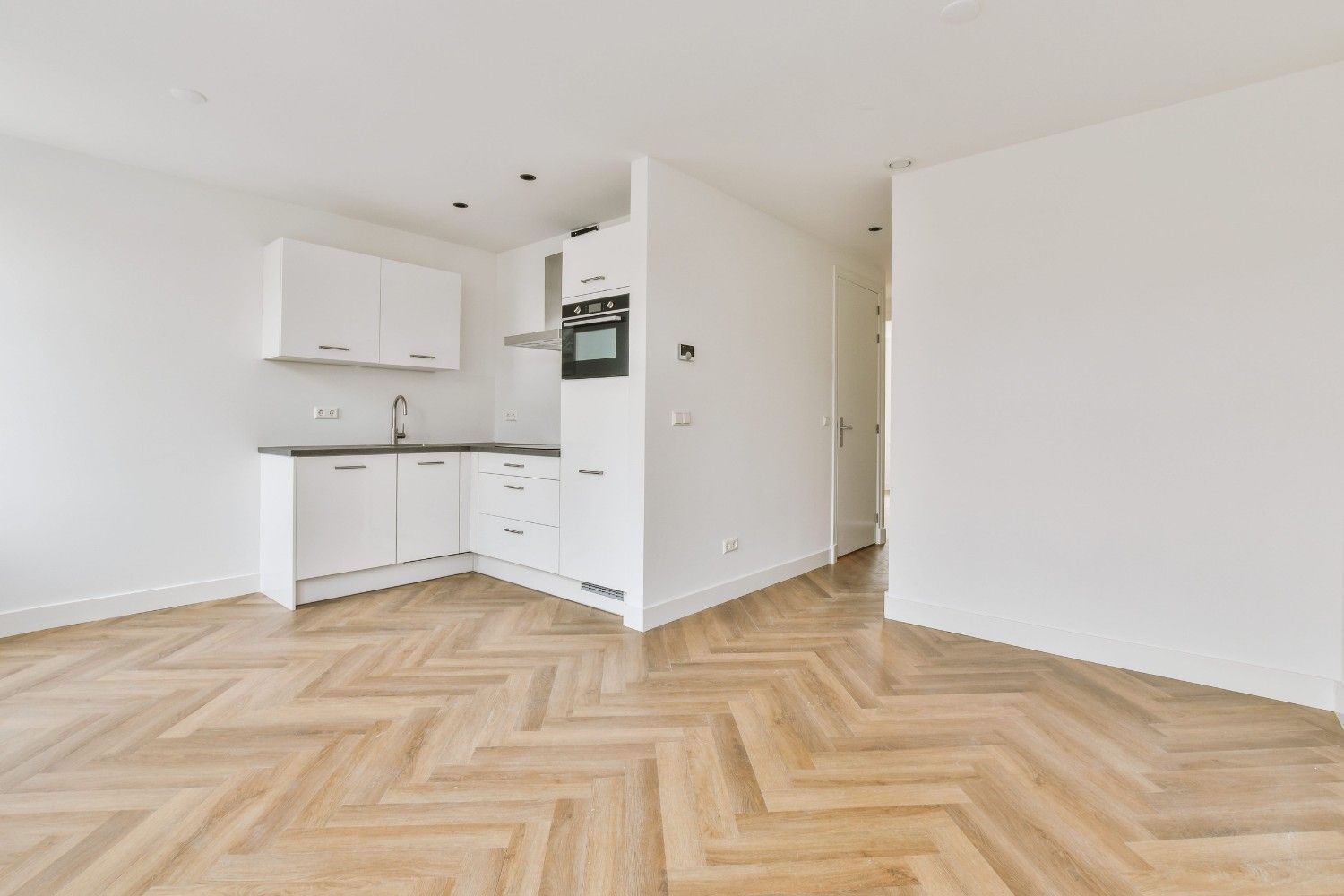 Apartamento luminoso y vacío con cocina americana blanca y suelo de madera en espiga.