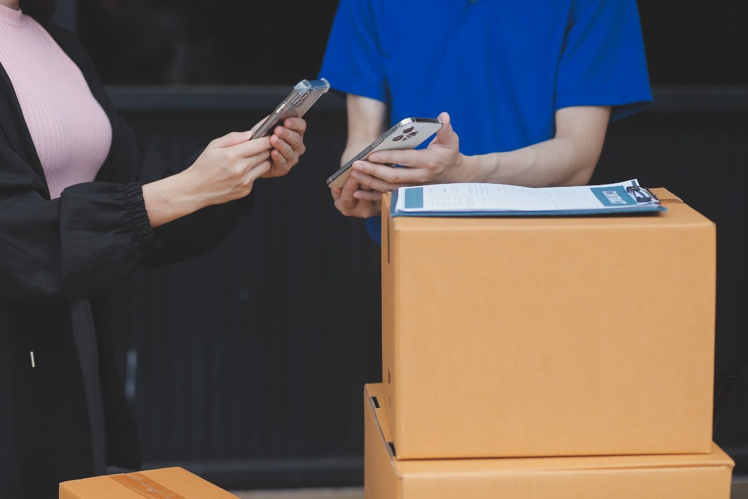 Una persona le entrega un teléfono inteligente a un empleado en un mostrador junto a cajas de cartón apiladas y un portapapeles.