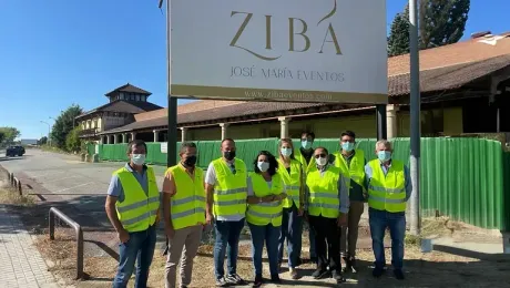 Un grupo de personas que llevan chalecos amarillos y máscaras están de pie frente a un cartel.