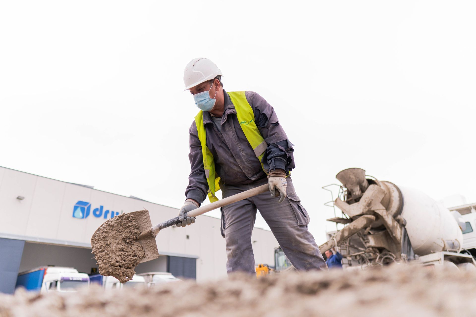 Un trabajador de la construcción que lleva una máscara está cavando con una pala.