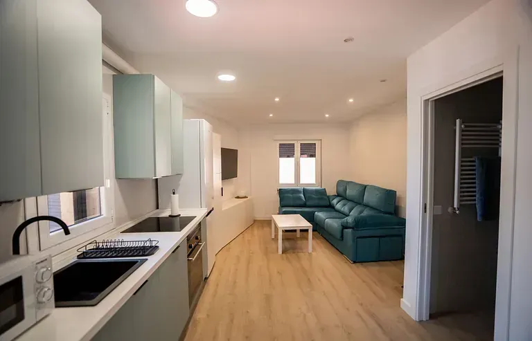Una sala de estar con un sofá azul y una cocina.