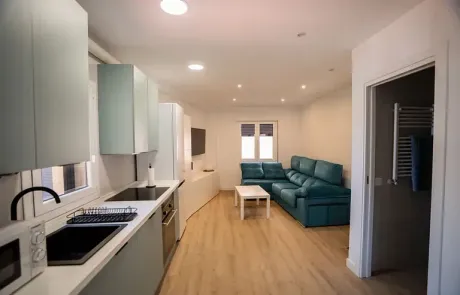 Una sala de estar con un sofá azul y una cocina.
