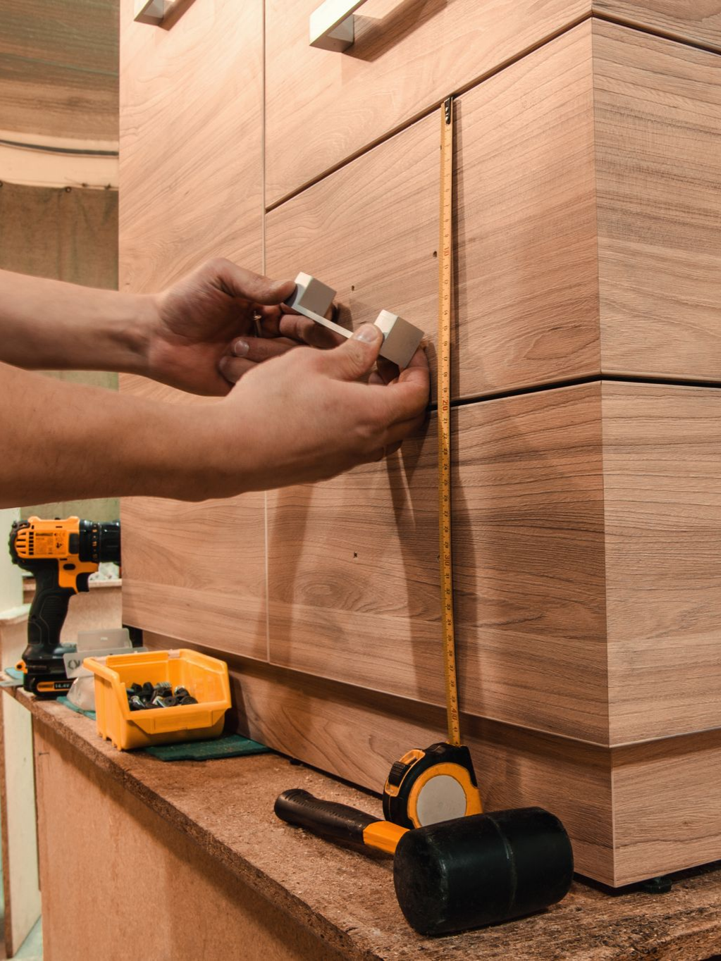 Personne installant une poignée de tiroir sur une armoire en bois à l'aide d'un mètre ruban. Outils intégrés au cadre.
