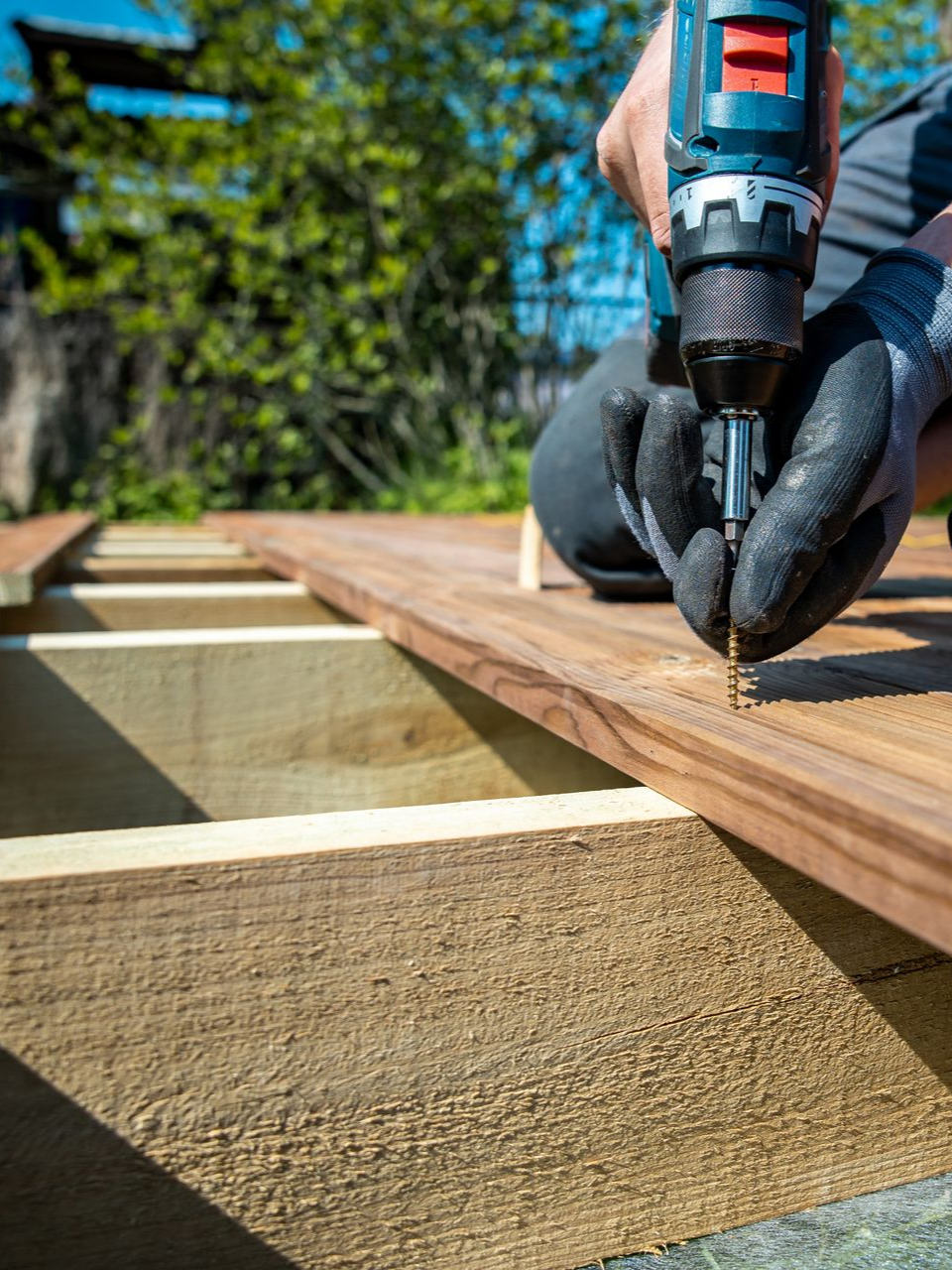 Un homme vissant les lattes de bois pour la fabrication d'une terrasse