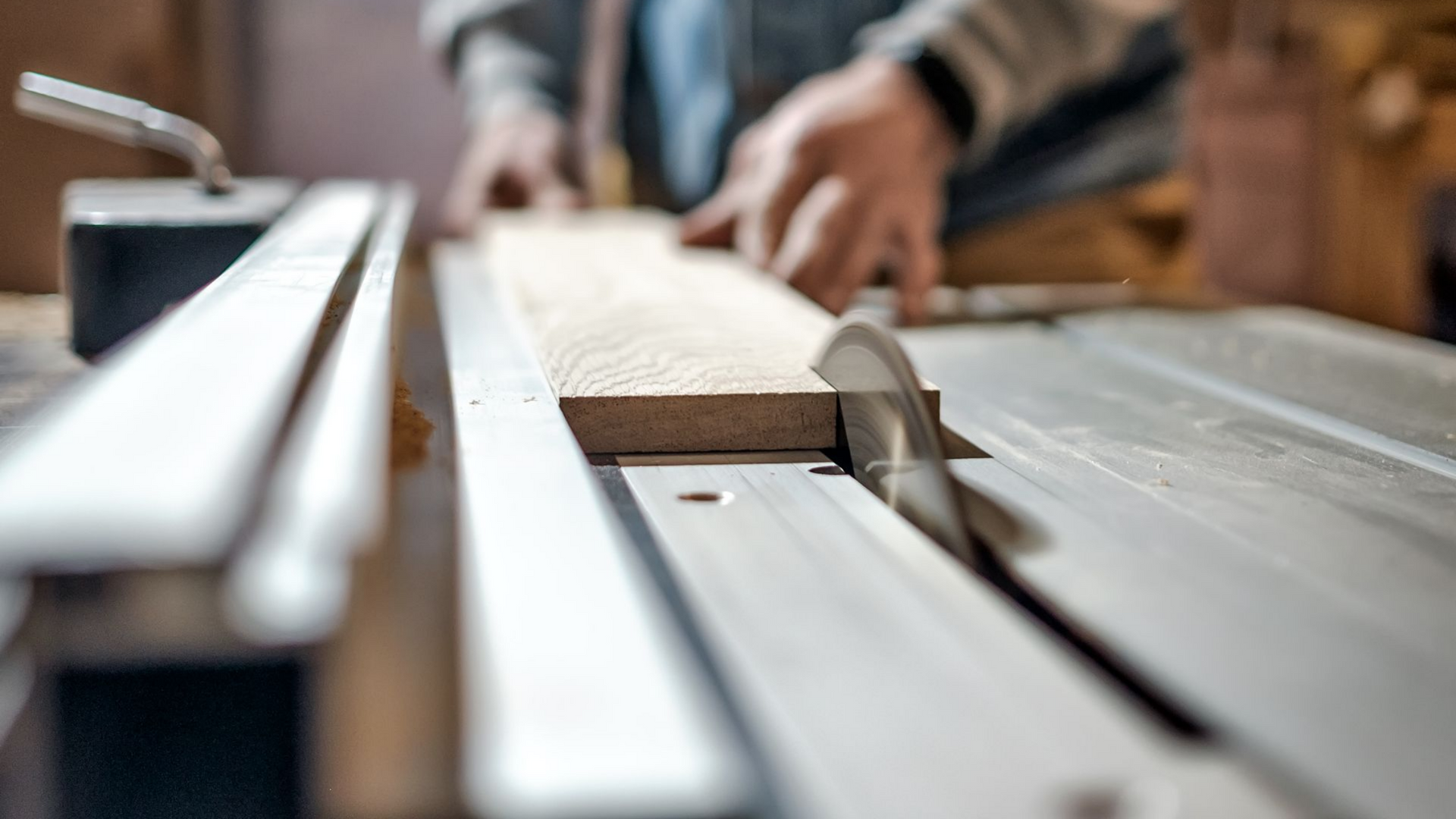Personne utilisant une scie circulaire pour couper une planche de bois dans un atelier.