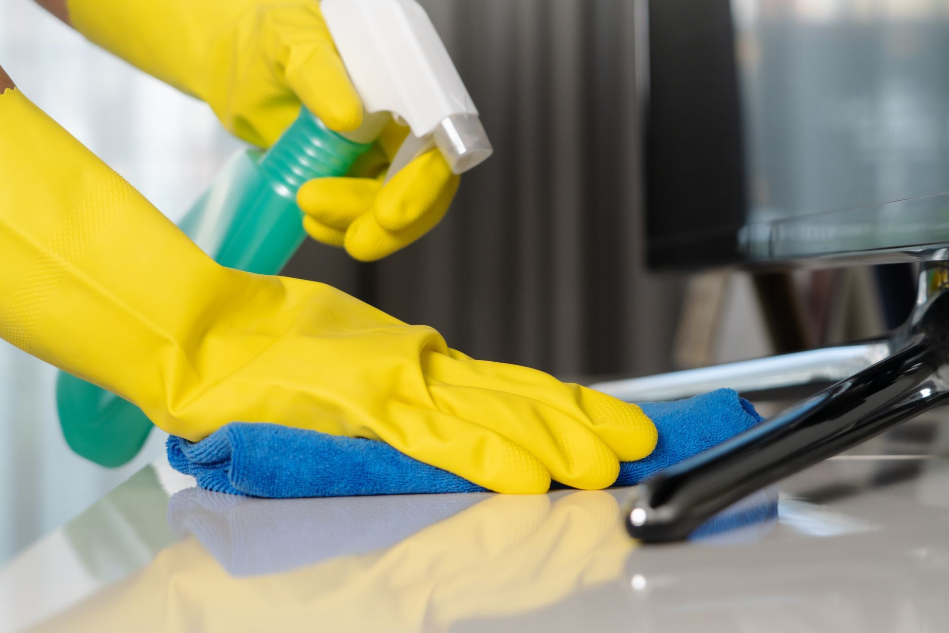 Una persona que lleva guantes amarillos está limpiando una mesa con un paño y una botella de spray.