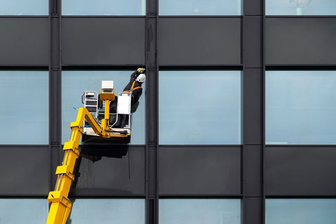 Un hombre está limpiando las ventanas de un edificio con una grúa.
