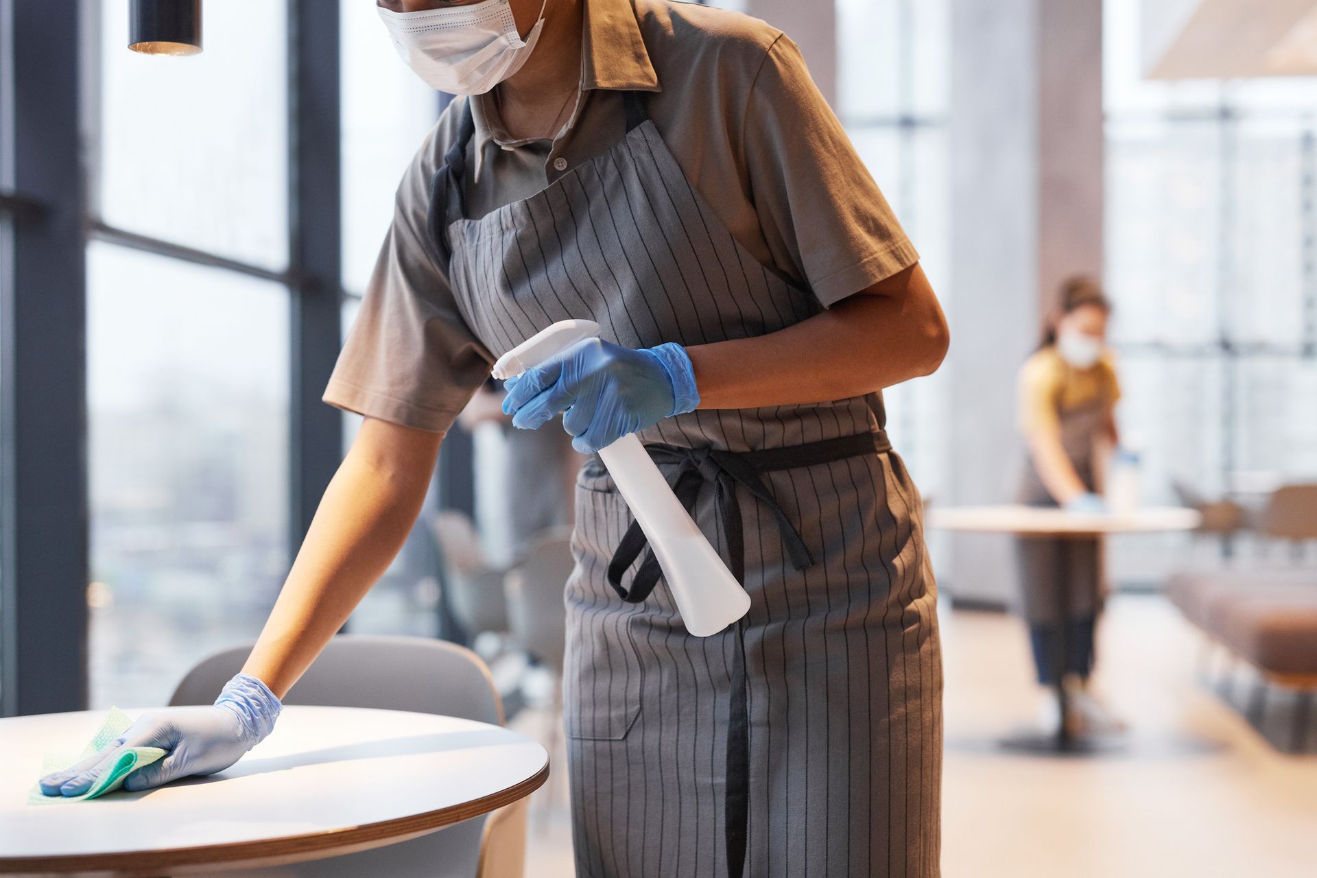 Una mujer que lleva una mascarilla y guantes está limpiando una mesa en un restaurante.