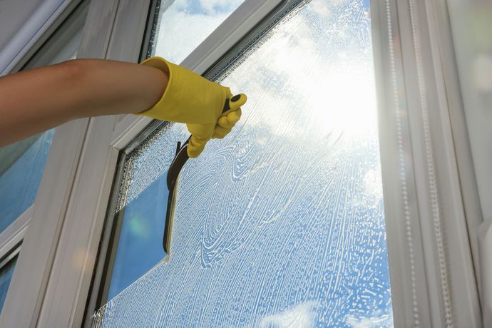 Una persona que lleva guantes amarillos está limpiando una ventana con una escobilla de goma.