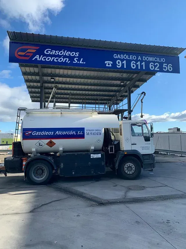 Un camión de gasolina está estacionado bajo un toldo en una gasolinera.