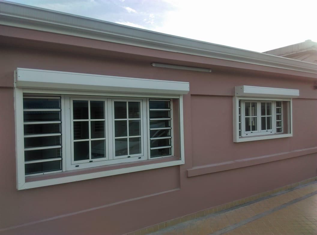 Bâtiment rose avec deux fenêtres à cadre blanc, chacune munie de volets blancs fermés.