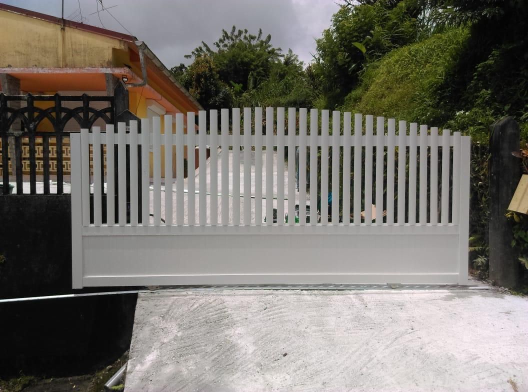 Portail blanc à lattes verticales sur une allée en béton, devant un bâtiment aux accents jaune et noir.