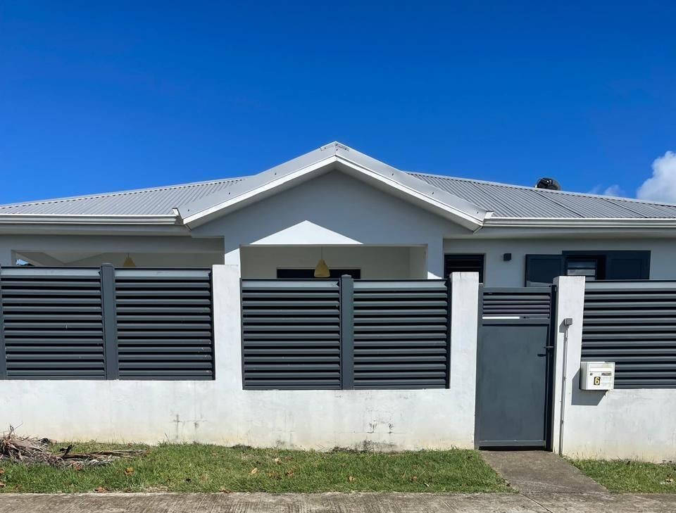 Une maison blanche avec une clôture, un portail et un toit en lattes grises.