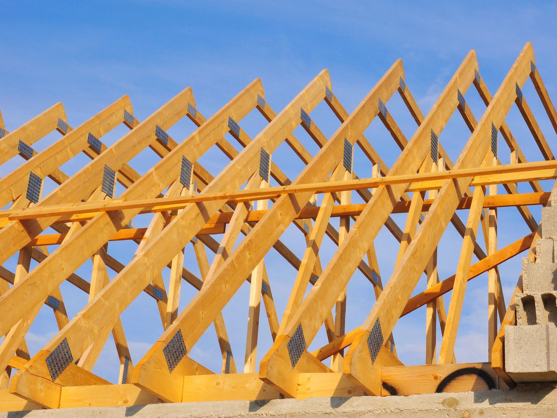 Charpente de toit en bois en construction, sur fond de ciel bleu.