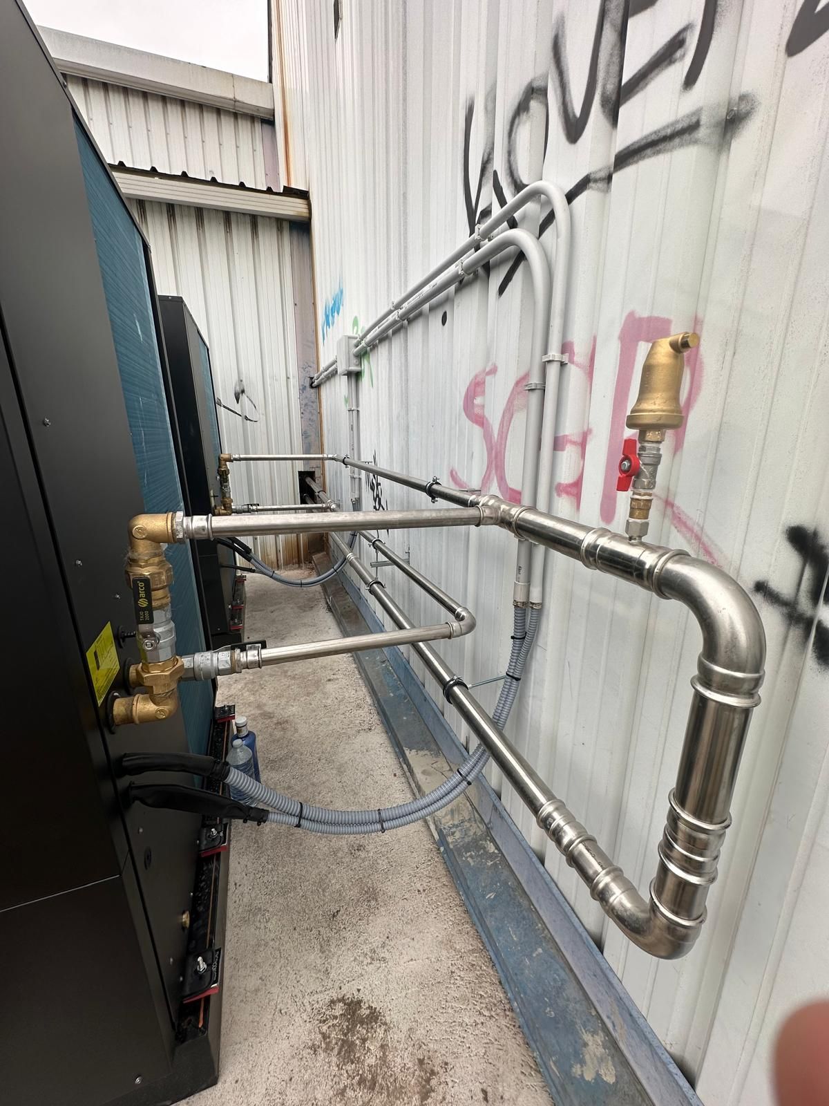 Tuberías y válvulas a lo largo de una pared blanca. Una máquina negra a la izquierda.