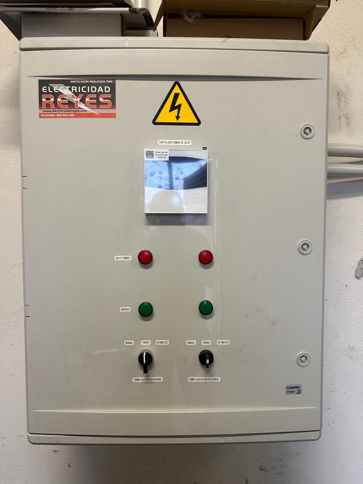 Panel de control eléctrico gris con botones, interruptores y señal de advertencia, montado en una pared.