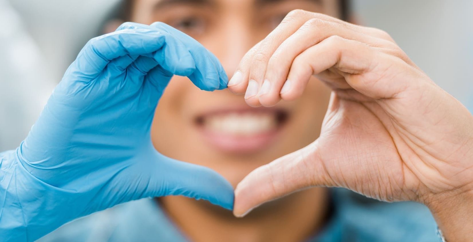 Ein Mann mit blauen Handschuhen formt mit seinen Händen ein Herz | Zahnmedizin am Neckar