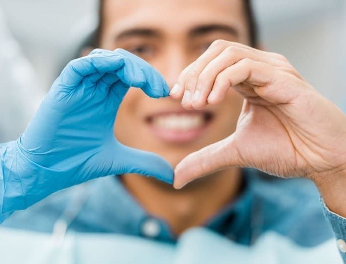Ein Mann mit blauen Handschuhen formt mit seinen Händen ein Herz | Zahnmedizin am Neckar