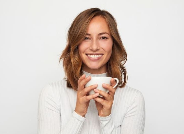 Eine Frau hält eine Tasse Kaffee in der Hand und lächelt | Zahnmedizin am Neckar